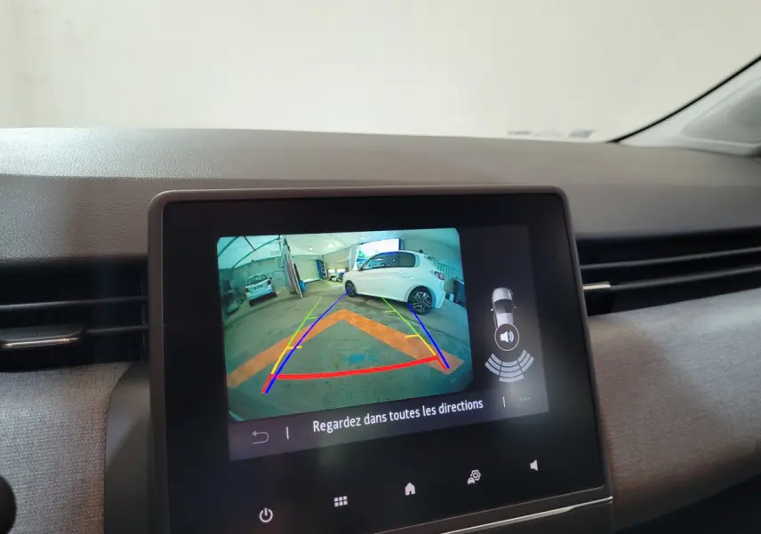 Écran tactile central montrant la caméra de recul avec une voiture blanche en arrière-plan dans un garage.