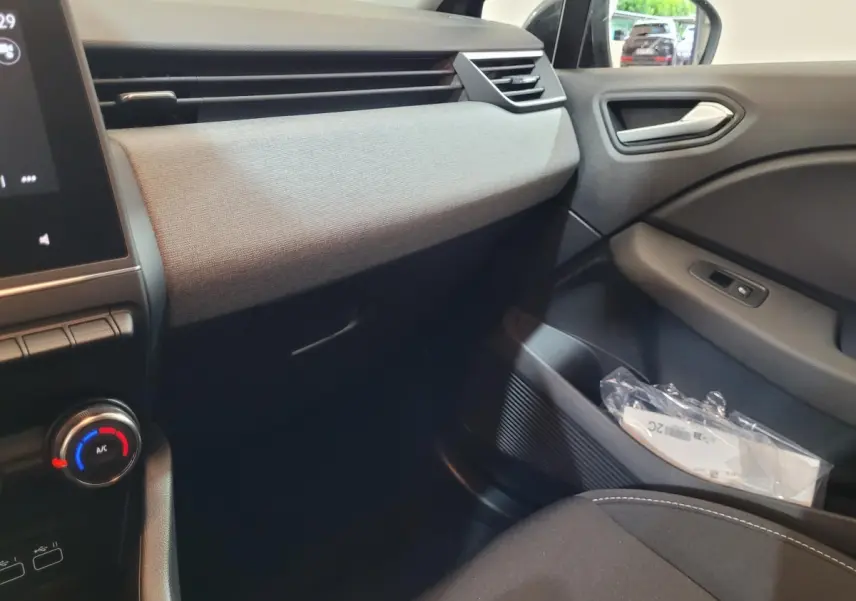 Intérieur côté passager de la Renault Clio gris foncé 2025, avec tableau de bord texturé et commandes de porte visibles.