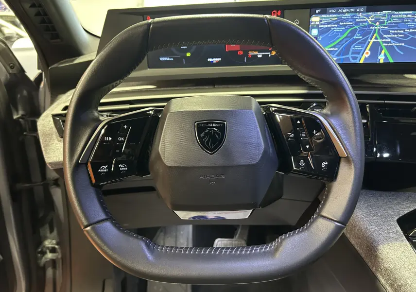 Vue rapprochée du volant cuir noir du Peugeot 5008 2025 avec tableau de bord numérique et écran de navigation intégré.