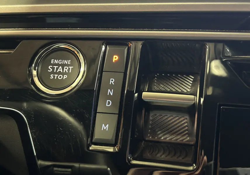 Gros plan sur la console centrale noire du Peugeot 5008 hybride 2025, avec bouton start/stop et sélecteur de boîte automatique.