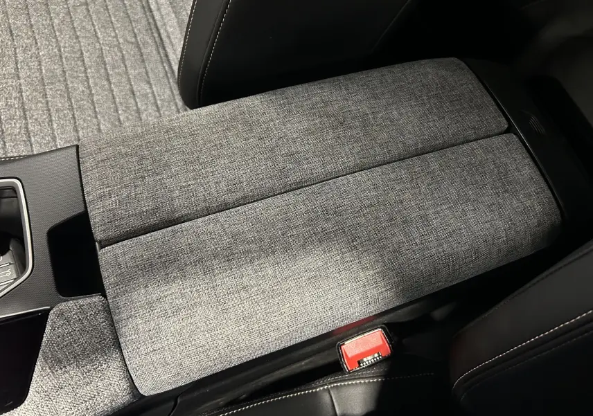 Détail de l'accoudoir central en tissu gris dans l'habitacle du Peugeot 5008 III Hybrid 145 e-DCS6 Allure.