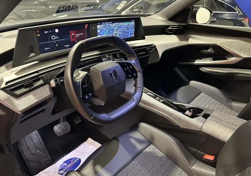 Intérieur du Peugeot 5008 2025 avec tableau de bord numérique et volant compact, sièges gris et finition tissu/cuir.