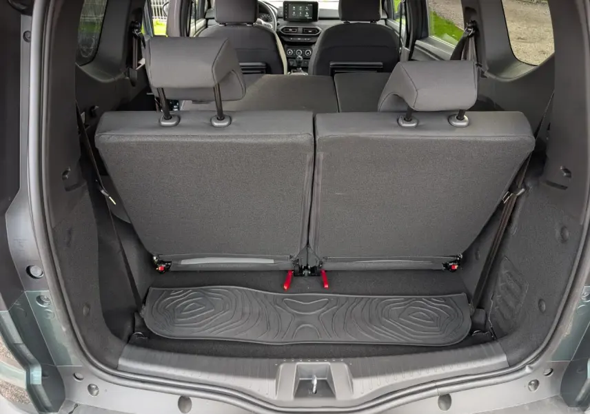 Vue arrière du coffre du Dacia Jogger vert métallisé 2025 avec sièges rabattus et tapis caoutchouc noir.