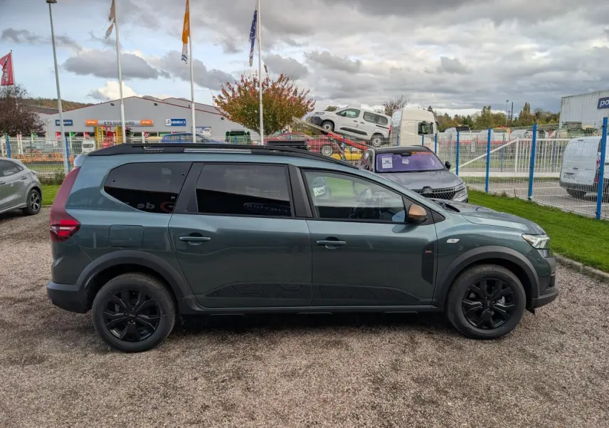 Profil côté gauche du Dacia Jogger 2025 vert métallisé avec jantes noires et barres de toit noires.