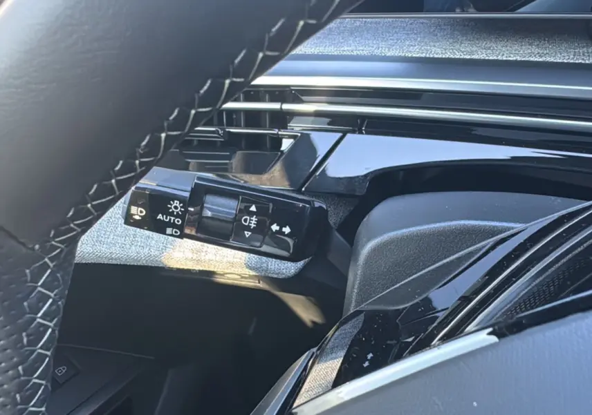 Détail du commodo d'éclairage à gauche du volant cuir dans l'habitacle du Peugeot 3008 gris titane 2025.