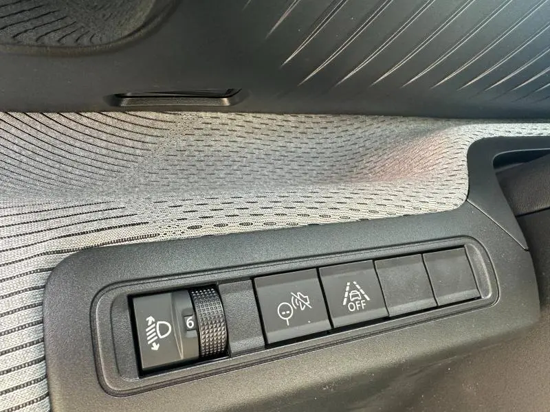 Gros plan sur les commandes de réglage des phares et d'aide à la conduite sur la porte côté gauche du Citroën C3 Aircross gris Mercury.