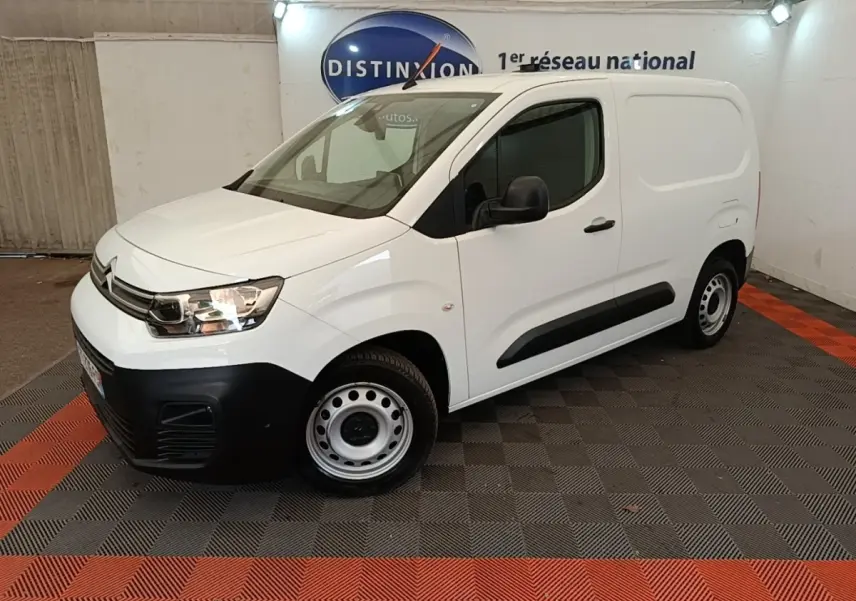Vue 3/4 avant droit d’un utilitaire Citroën Berlingo blanc avec pare-chocs noirs et jantes acier en intérieur showroom.