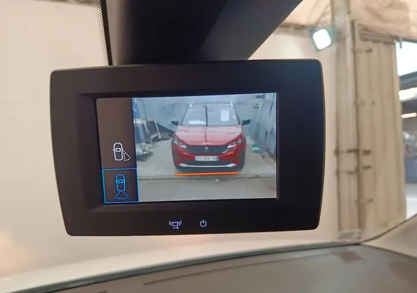 Écran de caméra de recul montrant une voiture rouge vue de face dans un garage, prise depuis l'intérieur.