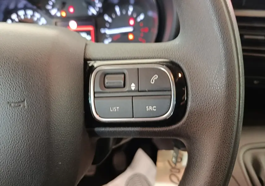 Gros plan sur les commandes gauche du volant noir du Citroën Berlingo 2020 avec tableau de bord flou en arrière-plan.