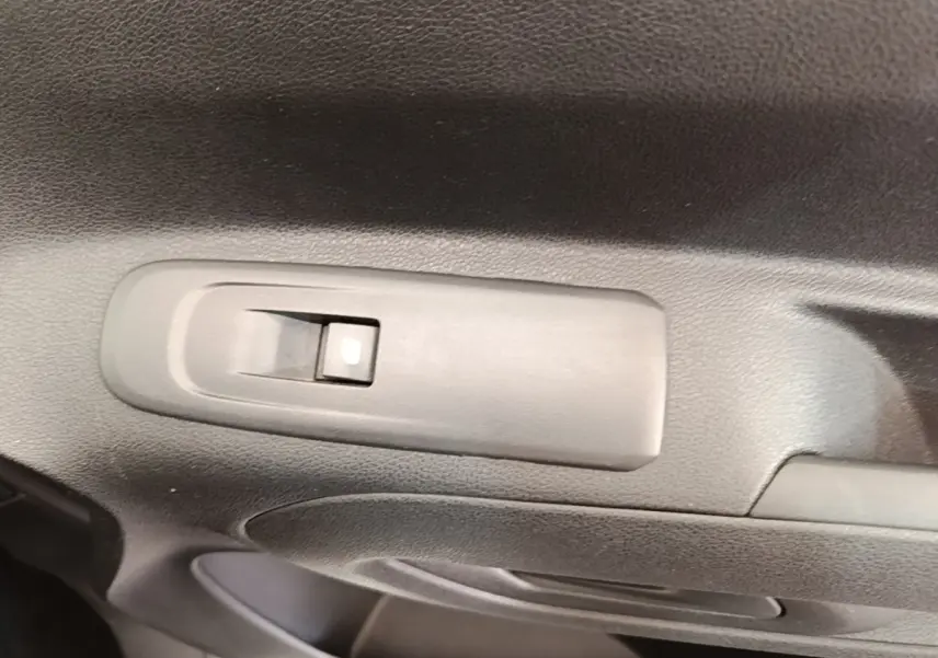 Gros plan sur le bouton de commande de la vitre électrique côté conducteur dans l'intérieur noir du Citroën Berlingo blanc.