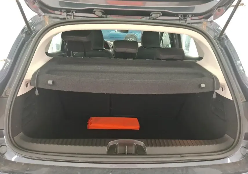 Coffre ouvert vu de l'arrière d'une Renault Clio gris foncé, avec une trousse de secours orange visible à l'intérieur.
