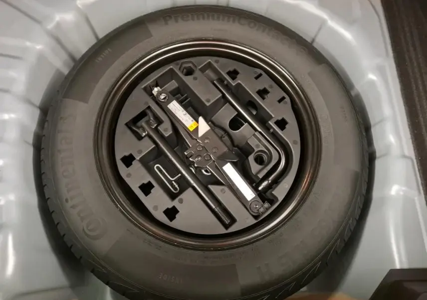 Gros plan sur la roue de secours et le kit d'outils rangés dans le coffre d'une Renault Clio gris foncé.