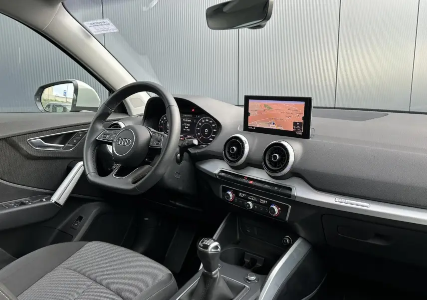 Vue intérieure côté conducteur de l'Audi Q2 30 TFSI S-Line 2024, avec volant cuir, écran navigation et levier de vitesse manuel.