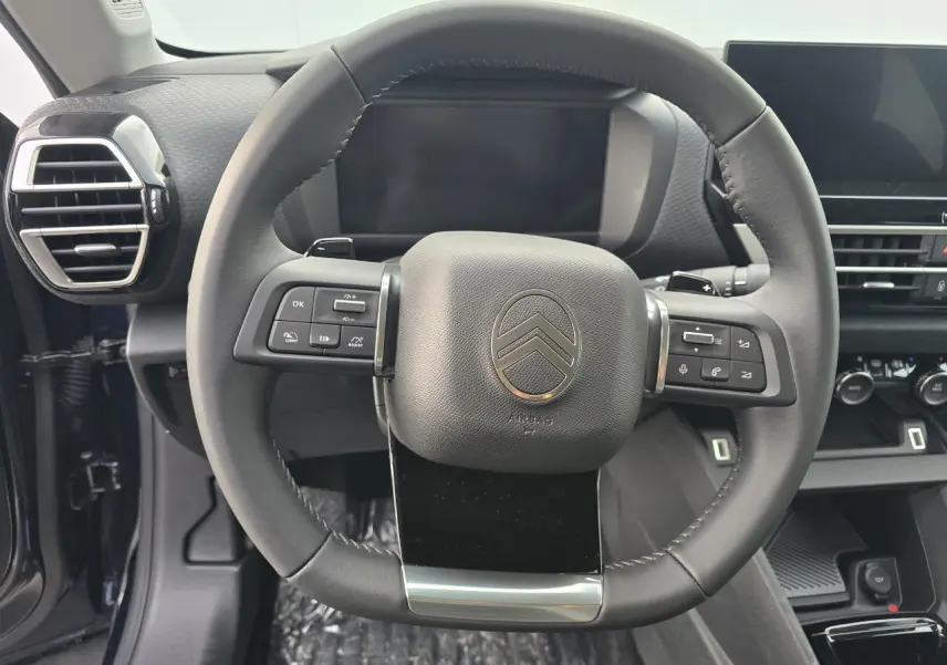 Volant cuir noir Citroën C4 2025 vu de face avec commandes intégrées et tableau de bord numérique en arrière-plan.