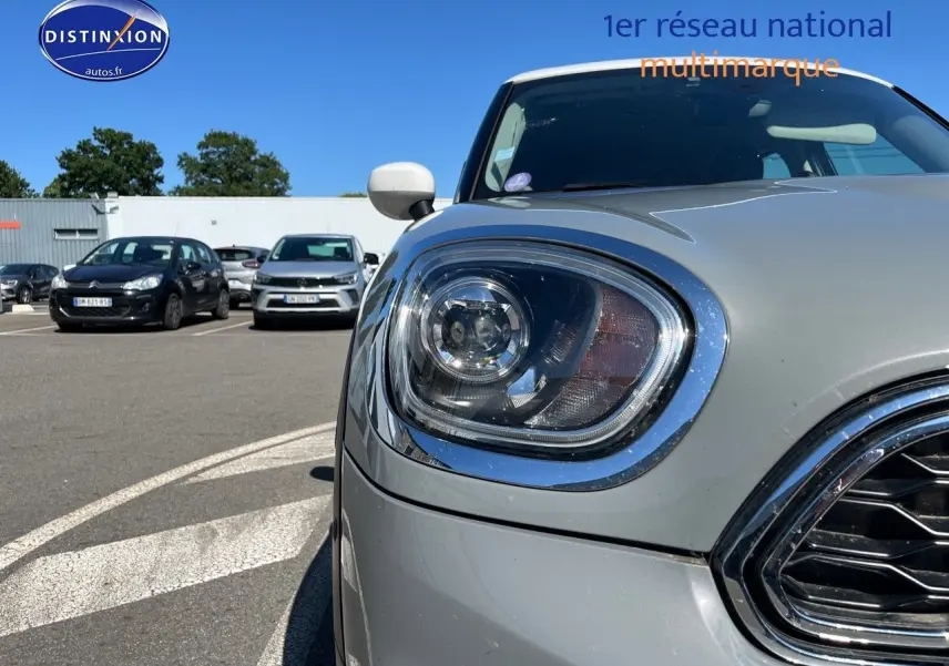 Gros plan sur le phare avant gauche et la calandre chromée d’une MINI Countryman Moonwalk Grey, toit blanc.