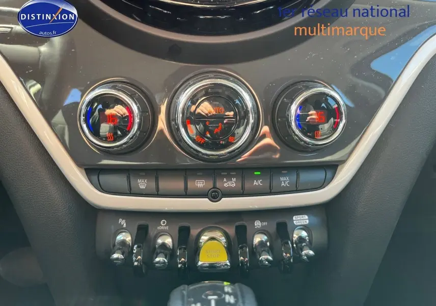 Vue intérieure centrée sur la console centrale du MINI Countryman Cooper SE avec commandes de climatisation et bouton Start/Stop jaune.