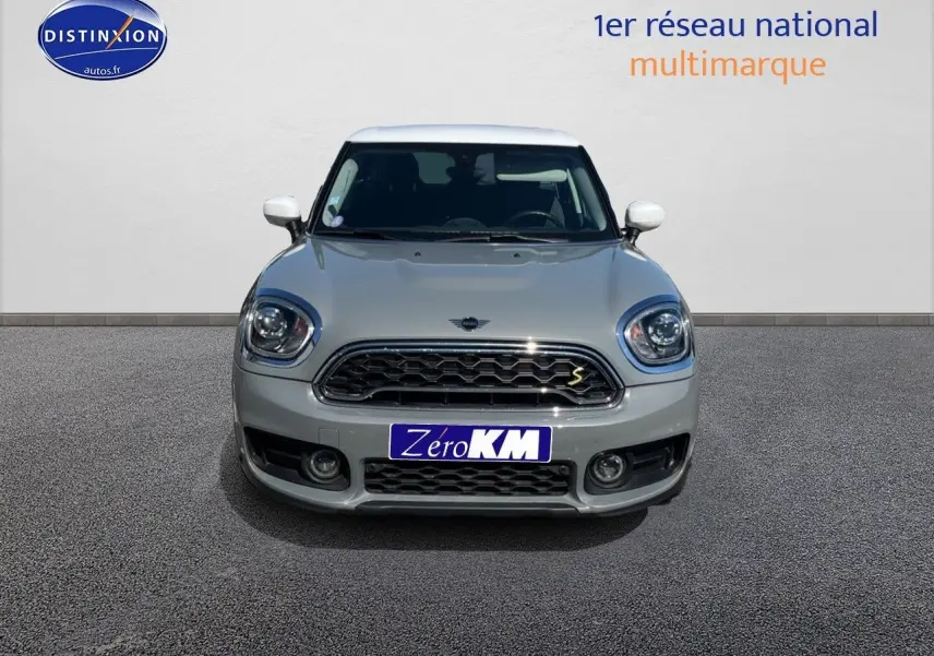 Vue avant d'une MINI Countryman hybride rechargeable Moonwalk Grey avec toit et rétroviseurs blancs, calandre chromée.