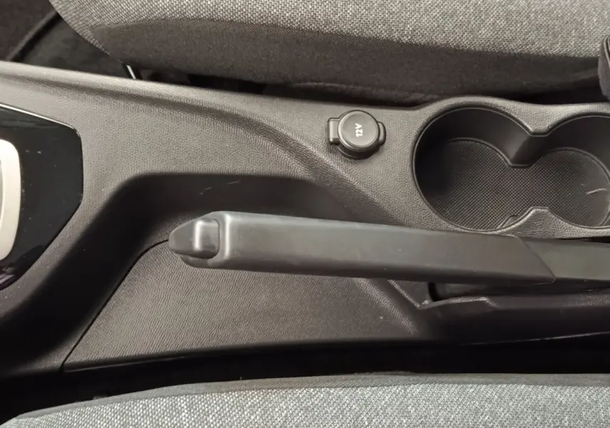 Vue rapprochée de la console centrale noire avec frein à main manuel et prise 12V du Peugeot 2008 blanc.