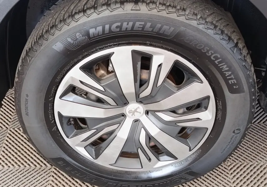 Gros plan sur la roue avant droite d’un Peugeot 2008 blanc, avec jante alliage et pneu Michelin CrossClimate.