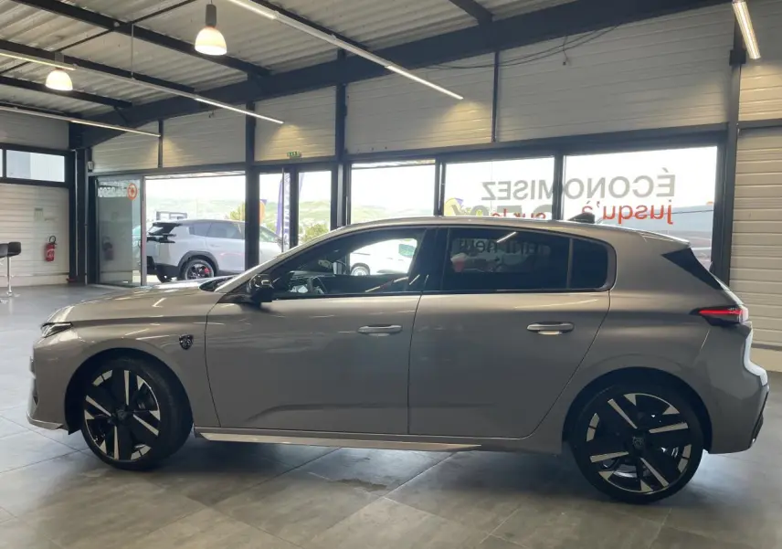 Profil droit de la Peugeot 308 GT 2026 gris Artense avec jantes alliage bi-tons et blason sur aile avant.