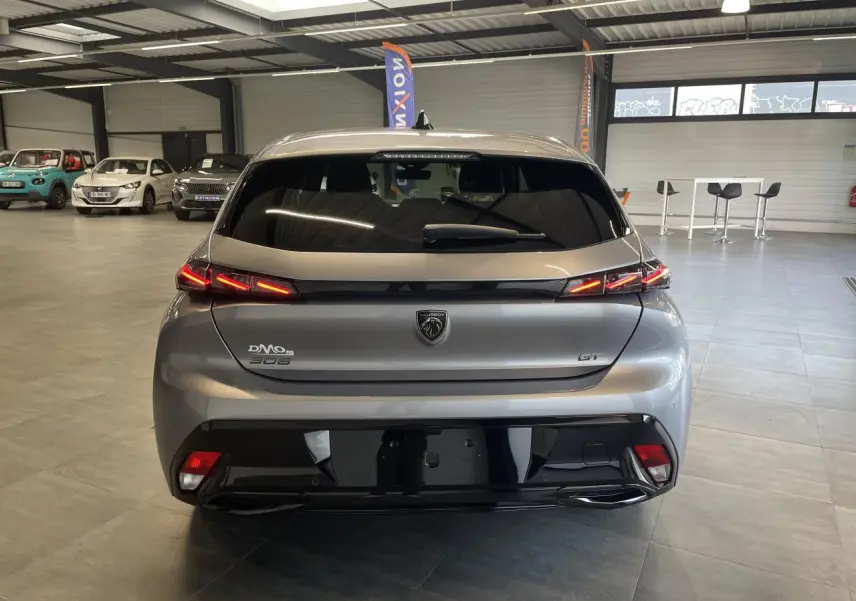 Vue arrière d'une Peugeot 308 GT gris Artense avec feux arrière LED 3 griffes et bandeau noir brillant en intérieur showroom.