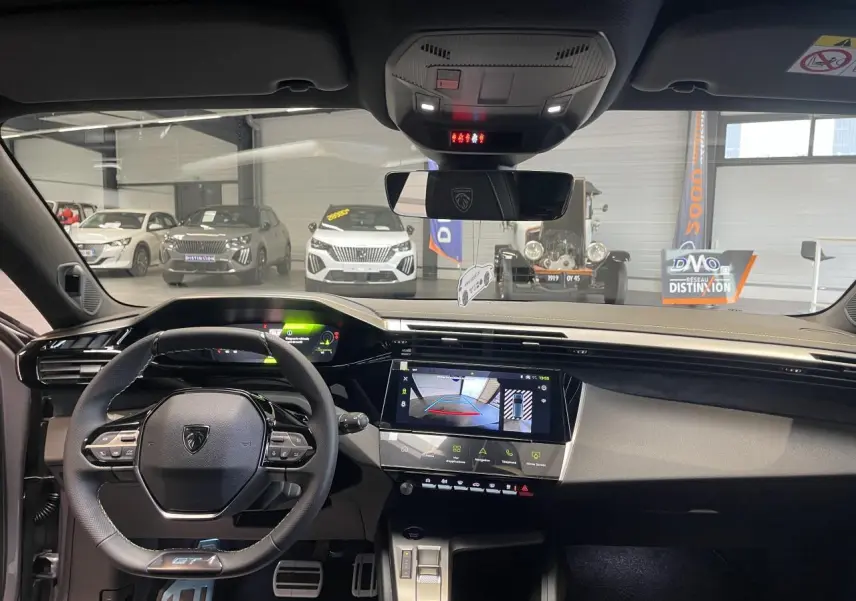 Vue intérieure avant de la Peugeot 308 GT 2026 gris Artense, avec volant compact GT et écran tactile central allumé.