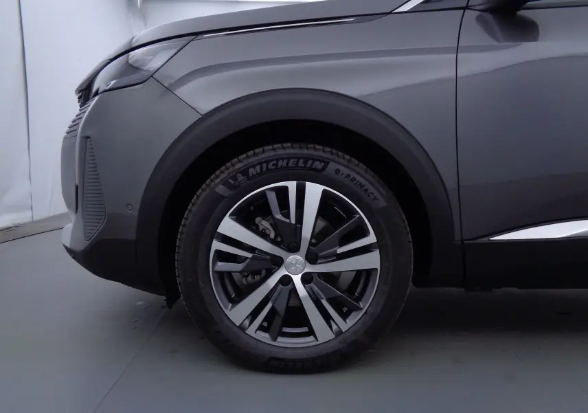 Gros plan sur la roue avant gauche et l'aile d'un Peugeot 5008 gris platinium métal, soulignant la jante alliage bicolore.