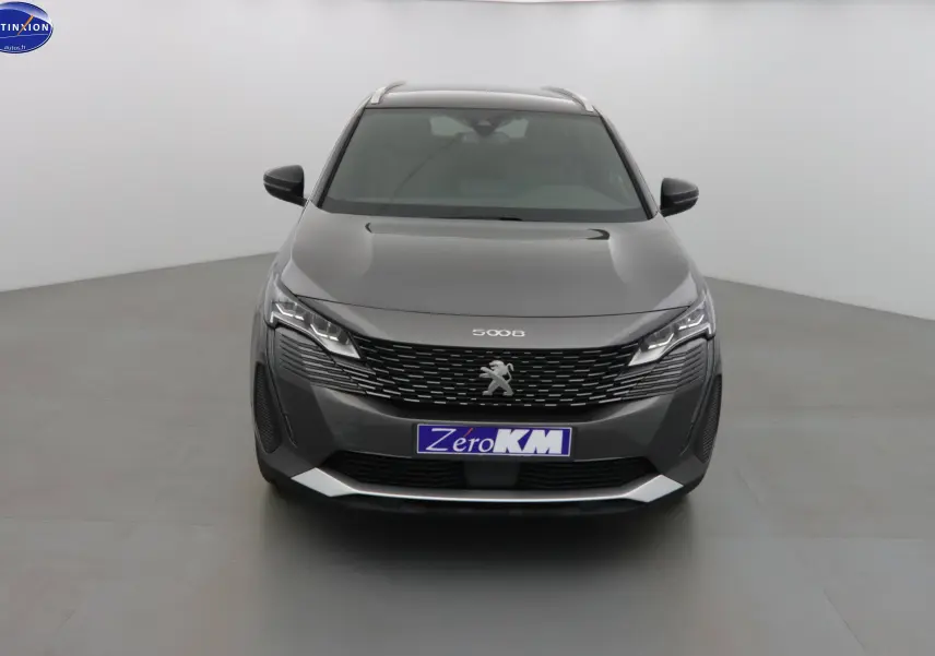 Vue frontale d'un Peugeot 5008 gris platinium métal avec calandre noire et phares LED allumés dans un studio.