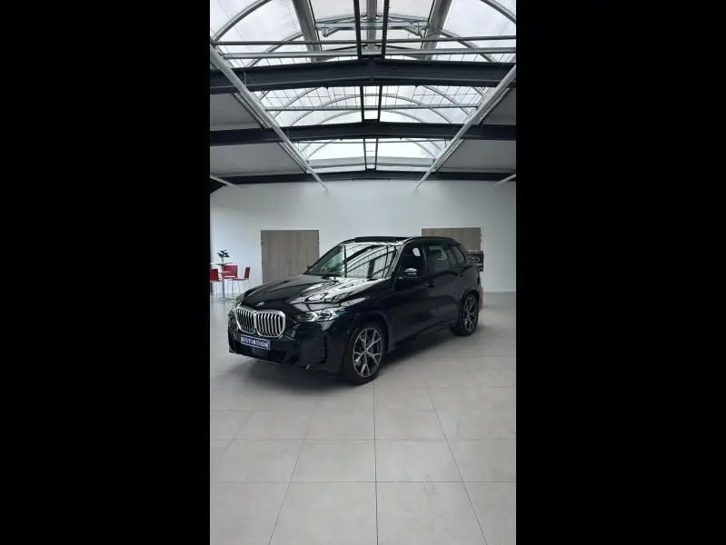 BMW X5 xDrive50e noir en 3/4 avant droit dans un showroom lumineux avec jantes alliage et calandre chromée.