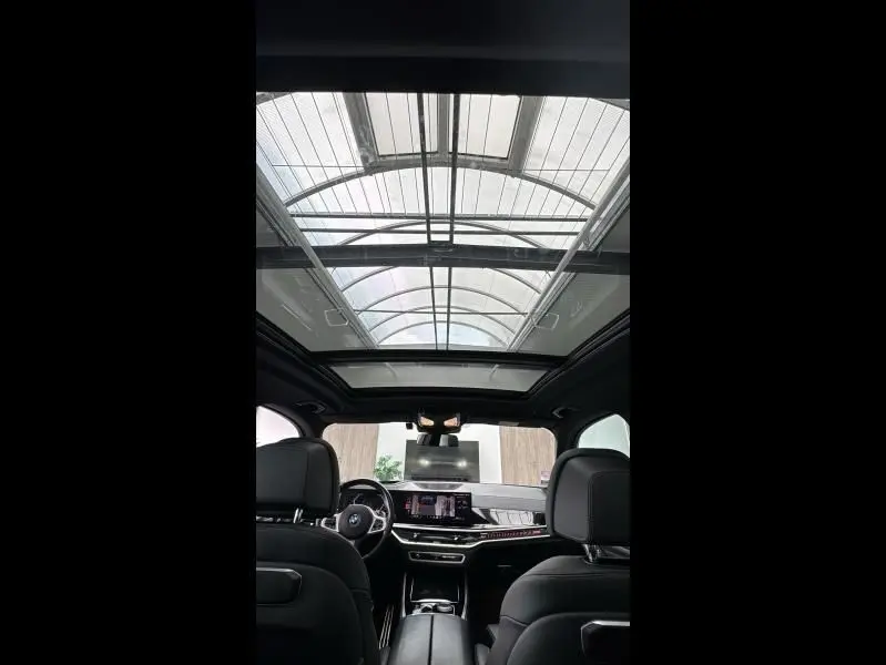 Intérieur noir du BMW X5 xDrive50e 2023 vu de l'arrière, avec toit ouvrant panoramique en verre et tableau de bord moderne.