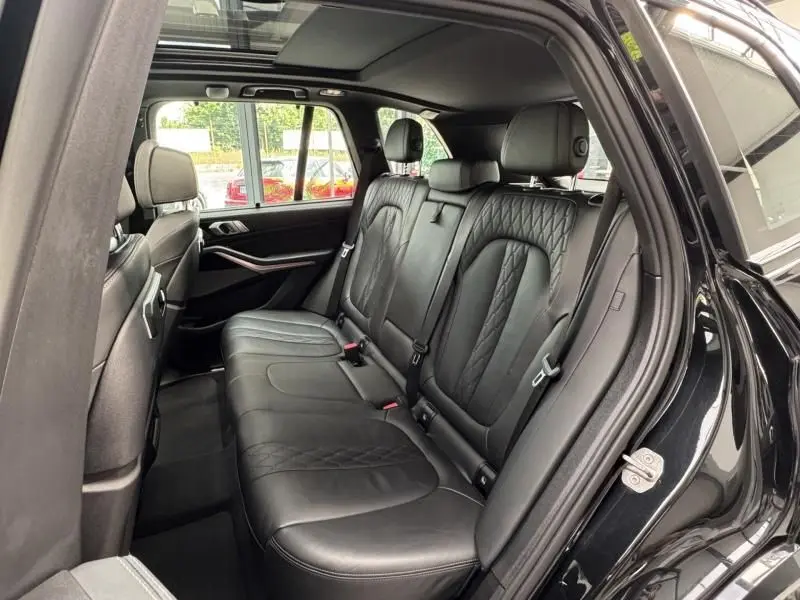 Vue intérieure arrière côté gauche du BMW X5 xDrive50e noir, montrant les sièges en cuir Merino avec surpiqûres raffinées.