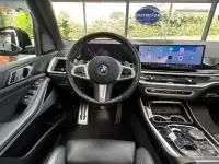 Vue intérieure avant du BMW X5 xDrive50e noir, volant cuir multifonction et large écran tactile central lumineux.