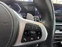 Gros plan sur les commandes audio au volant cuir du BMW X5 xDrive50e noir, avec tableau de bord et écran multifonction visibles.