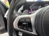 Gros plan sur les commandes du régulateur de vitesse au volant cuir d'un BMW X5 xDrive50e noir, intérieur moderne.