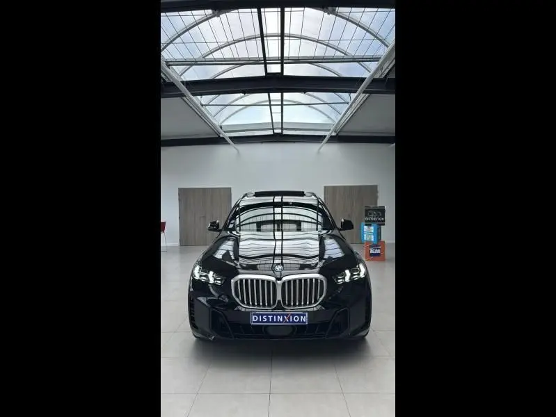 BMW X5 xDrive50e noir vu de face en intérieur, avec calandre chromée et phares LED allumés.