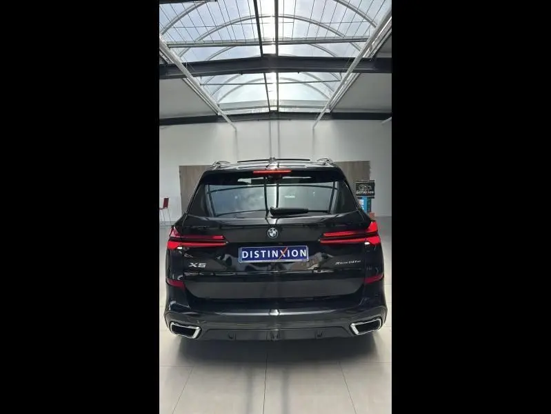 Vue arrière du BMW X5 xDrive50e noir métallisé avec feux LED et double sortie d’échappement chromée dans un showroom.