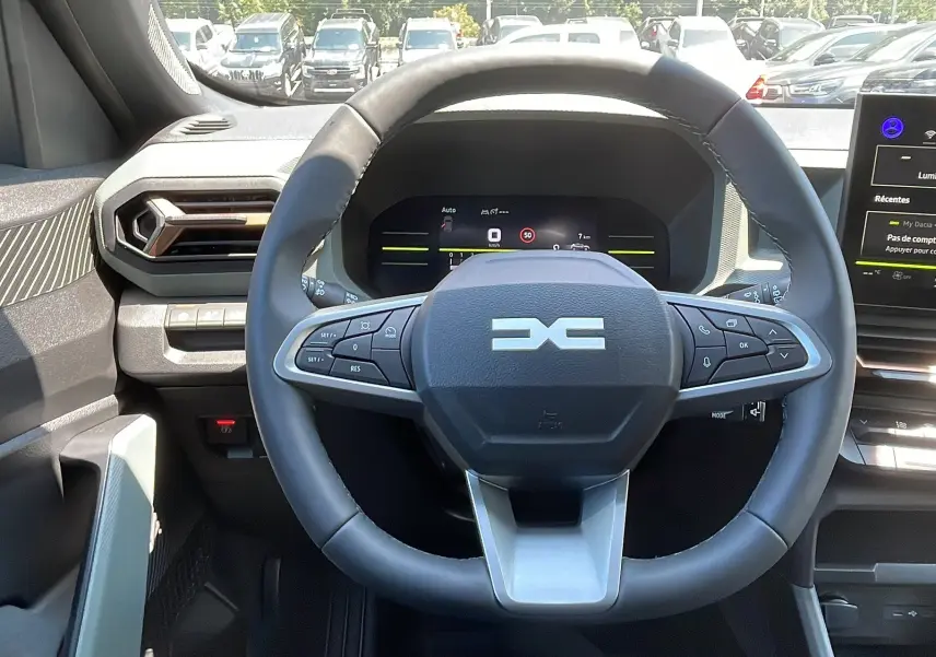Vue intérieure centrée sur le volant du Dacia Duster blanc 2025, avec tableau de bord numérique et écran tactile visible.