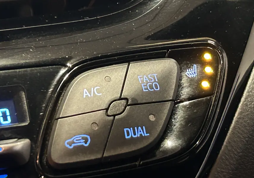 Gros plan sur les commandes de climatisation du Toyota C-HR Hybride noir, avec voyants de siège chauffant allumés.