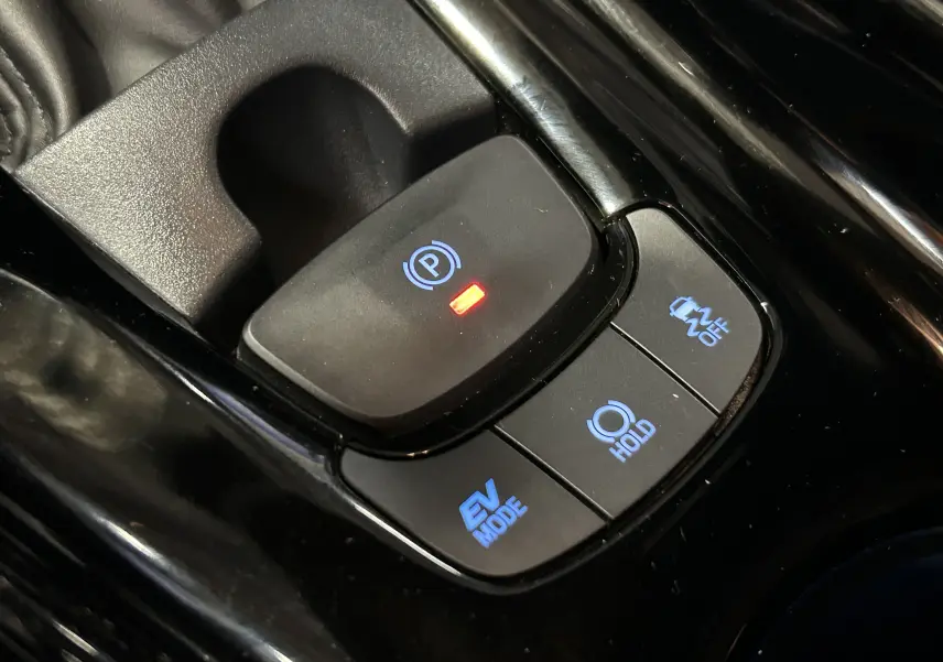 Gros plan sur les commandes de frein à main électronique et modes de conduite du Toyota C-HR Hybride noir métal 2021.