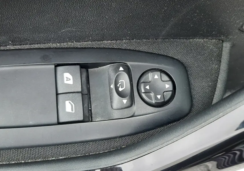 Gros plan sur les commandes de réglage des rétroviseurs et des vitres côté conducteur d'une Peugeot 208 bleu nuit 2019.