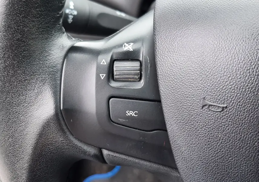 Gros plan sur les commandes du volant noir d'une Peugeot 208 bleu nuit 2019, avec bouton SRC et molette de volume.
