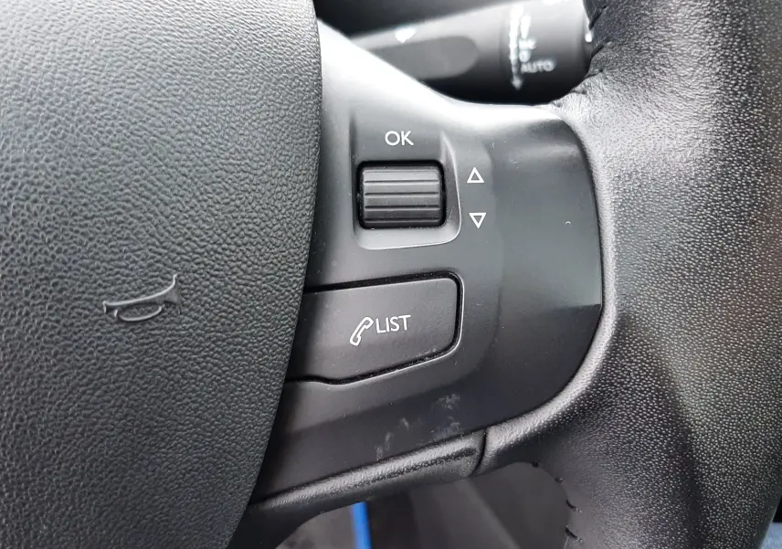 Gros plan sur les commandes gauche du volant noir de la Peugeot 208 bleu nuit, avec bouton OK et fonction liste d'appels.