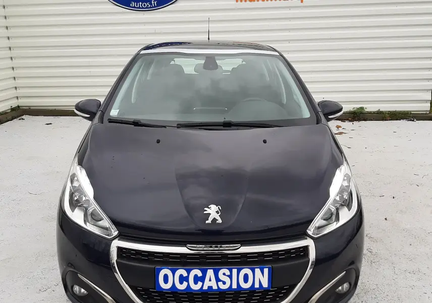 Peugeot 208 bleu nuit vue de face, avec calandre chromée et plaque "OCCASION" visible devant un mur blanc.