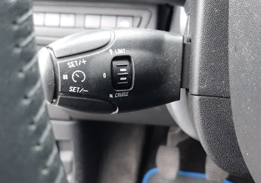 Gros plan sur la commande de régulateur de vitesse à gauche du volant dans l'habitacle noir d'une Peugeot 208 Bleu Nuit 2019.