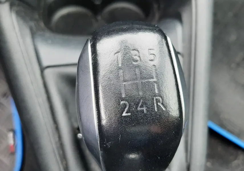 Gros plan sur le levier de vitesse noir manuel de la Peugeot 208 bleu nuit, montrant les positions des 5 rapports et la marche arrière.