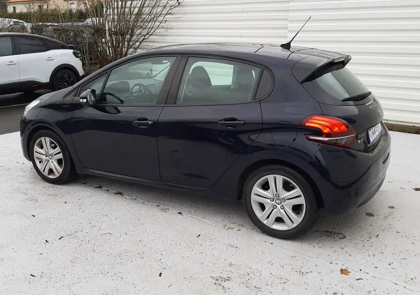 Peugeot 208 bleu nuit vue de profil côté gauche, avec feux arrière allumés et jantes alliage 16 pouces.