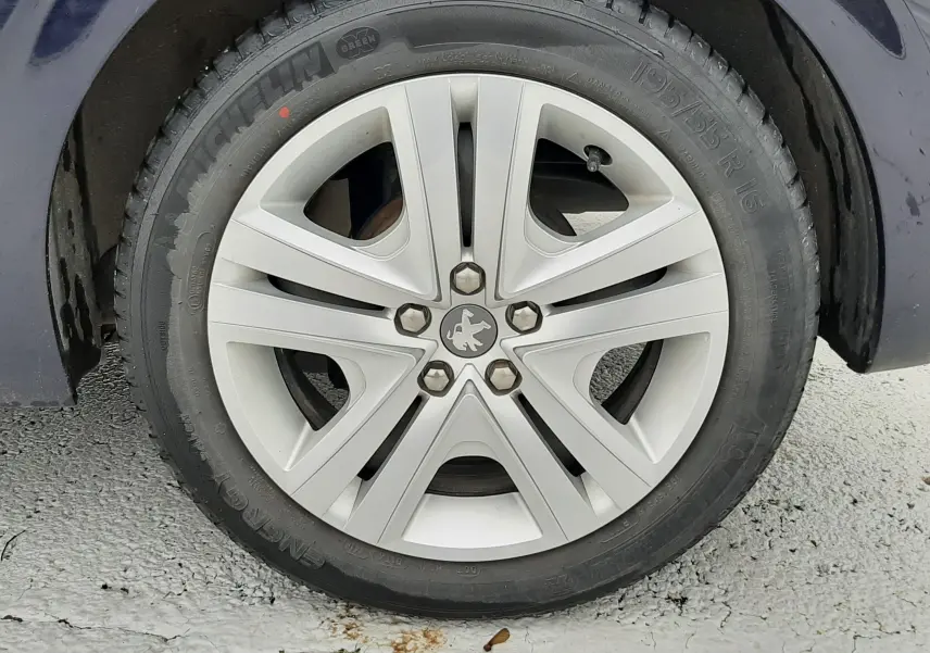 Gros plan sur la roue avant gauche d'une Peugeot 208 bleu nuit avec jante alliage cinq branches.