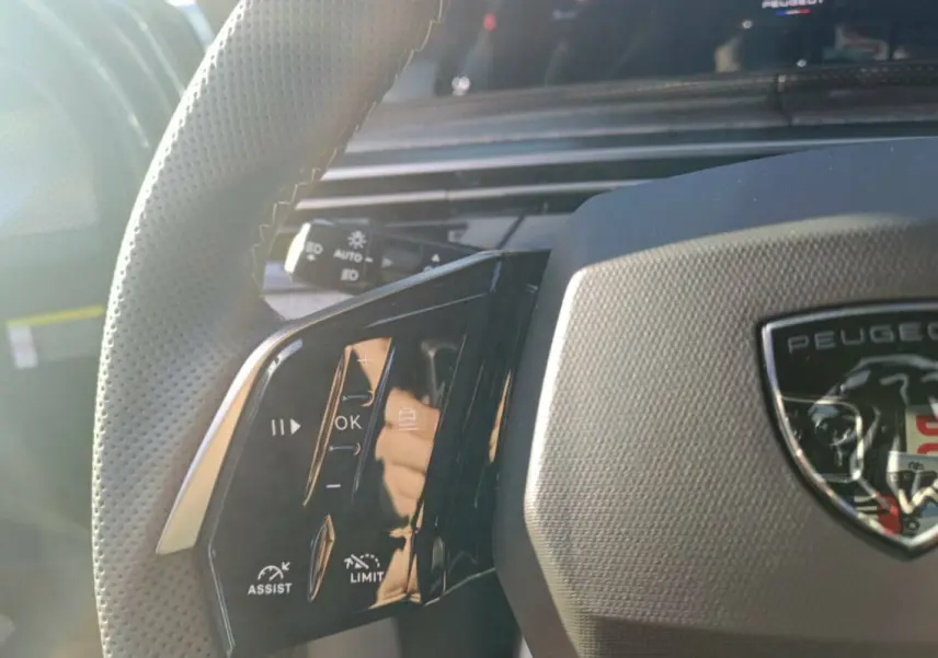 Gros plan sur le volant cuir multifonctions du Peugeot 3008 Hybrid 2025 avec logo et commandes intégrées.