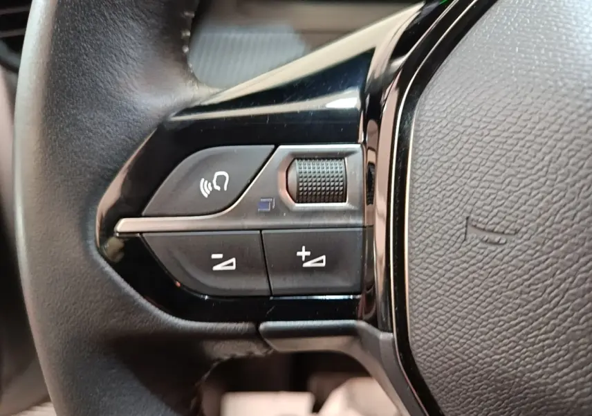 Gros plan sur les commandes gauche du volant cuir noir du Peugeot 208 gris clair, boutons multifonctions et molette.