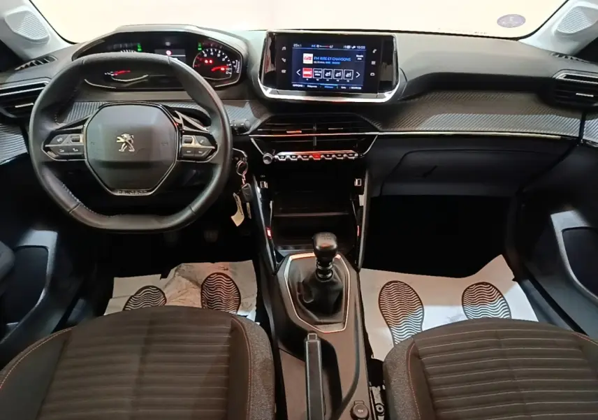 Vue intérieure avant du Peugeot 208 2023 avec volant cuir multifonctions, écran tactile central et boîte manuelle.